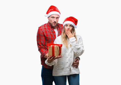 年轻夫妇在爱戴着圣诞帽子和持有目前在孤立的背景盖嘴与手震惊与羞愧的错误, 表达恐惧, 害怕沉默, 秘密概念