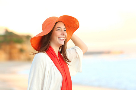 快乐的女人戴着橙色的图画帽子, 在海滩上沉思海洋