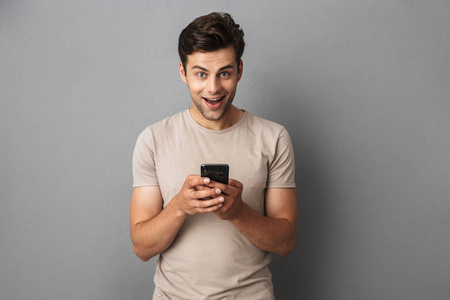 一个快乐的年轻人在 t恤上的肖像被孤立的灰色后台, 使用手机