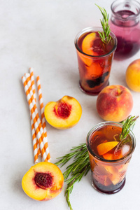 桃和迷迭香柠檬水或鸡尾酒在玻璃与新鲜的桃子在浅灰色背景。夏日冷饮