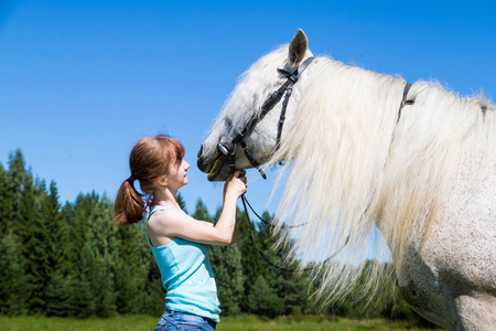 年轻女孩和白色马在自然在夏天晴朗的天
