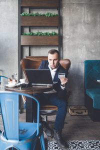 年轻, 现代和积极的商人坐在咖啡馆, 做他的工作在笔记本, 手机和平板电脑