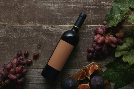 木桌上有空白标签新鲜葡萄和无花果的葡萄酒瓶的顶部视图