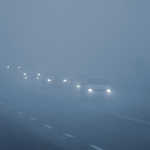 在雾中的汽车。恶劣的冬季天气和危险的汽车交通的道路上。轻型车辆在雾中