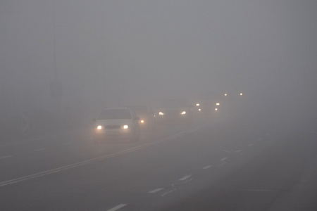 在雾中的汽车。恶劣的冬季天气和危险的汽车交通的道路上。轻型车辆在雾中