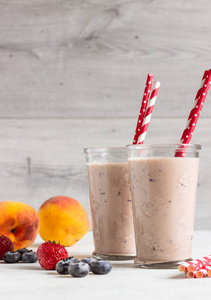 新鲜的自制草莓, 蓝莓和桃子在浅灰色背景下的玻璃杯。健康饮品或早餐