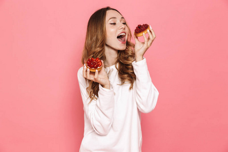 一个满意的年轻女子的肖像, 在粉红色的背景下吃糕点隔离