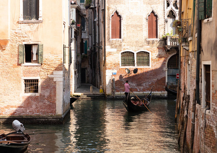 一只小船在威尼斯的旧建筑外墙上导航一个狭窄的通道, 那个男人穿着一件红色的脱衣服。