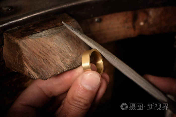 金匠手拿着一枚金戒指在木制工作台上, 用一个金属锉在上面工作, 与