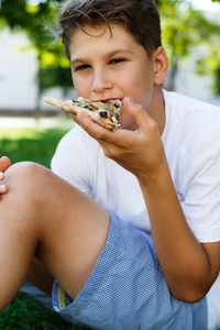 可爱的小男孩穿着白色 t恤, 吃比萨饼和微笑, 在夏日公园里玩得开心。