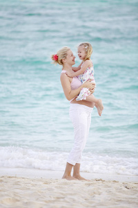 站在沙滩上时抱着婴儿的年轻孕妇