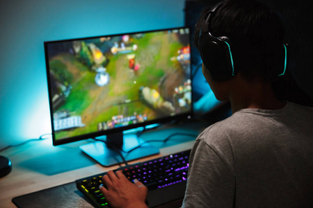 沉浸在十几岁的游戏玩家男孩的形象在黑暗的房间里玩视频游戏戴着耳机, 使用背光彩色键盘