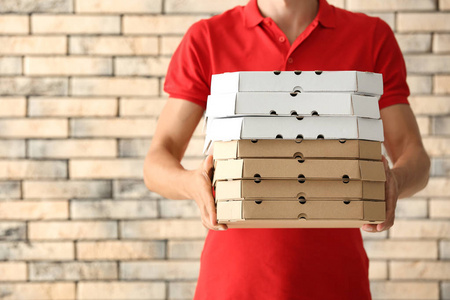 年轻人用比萨饼盒反对砖墙。食品配送服务
