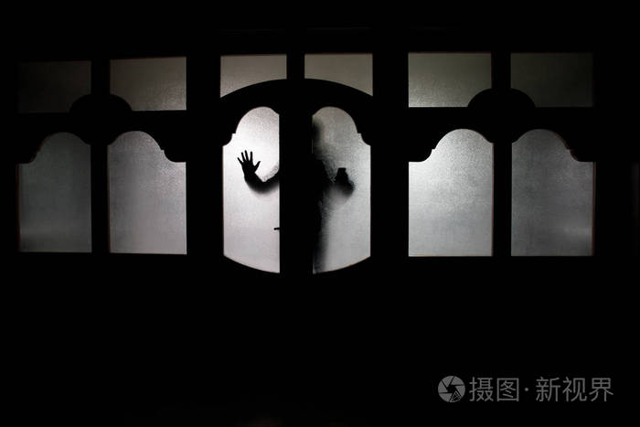 一个未知的影子身影在门通过一个封闭的玻璃门的剪影.