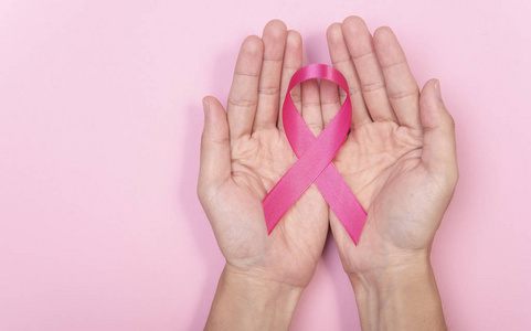 女性手捧粉红色缎带乳腺癌的粉红色背景。使用复制空间