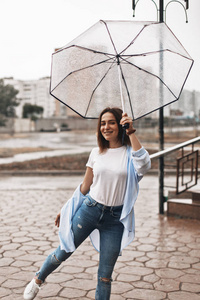 穿着蓝色衬衣的雨伞下有个漂亮的女人。女孩看起来很高兴。雨