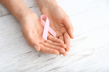妇女持有粉红色丝带在轻木背景。乳癌概念
