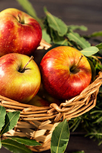 篮子里的甜苹果和绿叶围着, 在木桌上