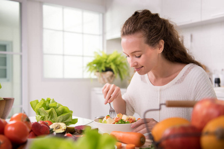 健康的年轻妇女在厨房里吃沙拉