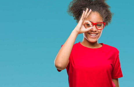年轻的美国黑人妇女戴眼镜在孤立的背景下做 ok 手势用手微笑, 眼睛看通过手指与愉快的面孔