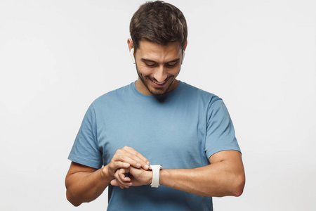 年轻英俊的男子身穿无线耳机和蓝色 t恤, 检查智能手表与触摸屏