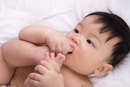 肖像的可爱的小亚洲男孩 6 个月大把他脚趾的脚在嘴里白色的床上，