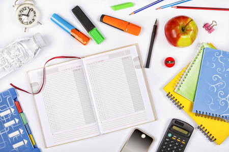 回到学校。打开笔记本的顶部视图与铅笔, 彩色图钉, 计算器, 手机和其他学校用品在一个白色的桌子上