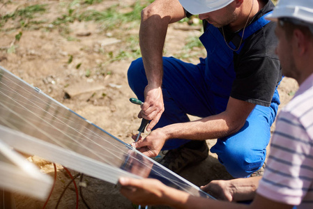 用螺丝刀将太阳能光电面板连接到夏季农村景观背景的金属平台上。独立的外部太阳能电池板系统安装理念