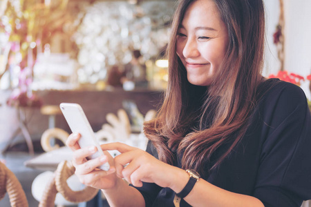 一个美丽的亚洲女人的特写图像在现代咖啡馆使用和看智能手机的笑脸