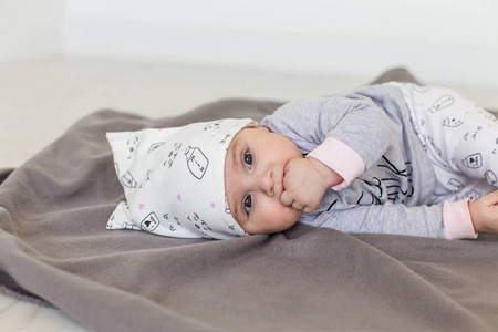 可爱的婴儿躺在灰色的毯子上, 并保持手指在他的嘴里。快乐童年概念