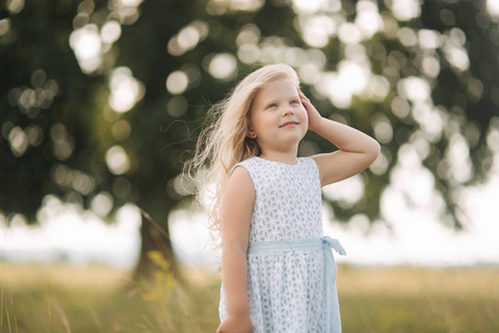 小女孩在天空蓝色礼服站立在领域在大树前面