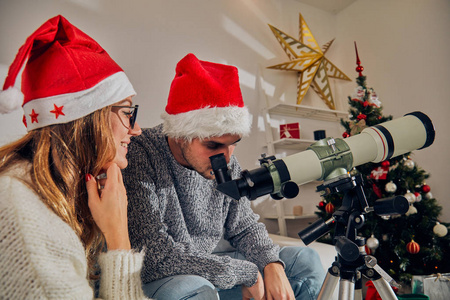 愉快的情侣朋友享受圣诞前夜新年前夜与望远镜在家里