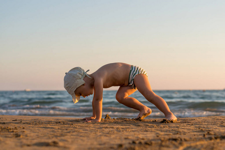 微笑小宝贝男孩在沙滩上在日落时运行时溅起水花在海