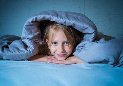 微笑和开朗甜美的小女孩看起来快乐躺在床上, 晚上或早晨在睡眠舒适快乐家庭和孩子的概念中感受快乐和休息