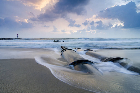 美丽的大自然，软波打混凝土排水管道在沙滩上在日出背景