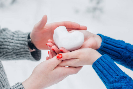 手在针织手套与雪的心脏在冬天的日子。爱的概念。背景