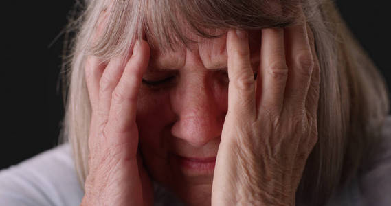 老年偏头痛患者在灰色背景下揉头的紧拍