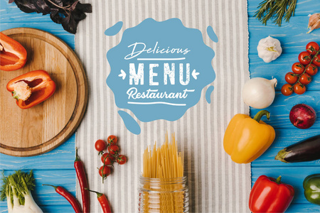 蓝色桌子上餐巾纸上未煮熟的意大利面和成熟蔬菜的顶部视图, 美味的菜单餐厅刻字