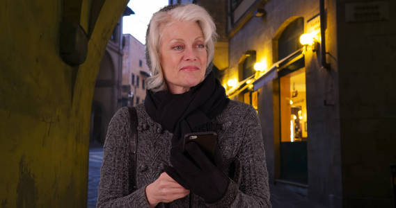 高级女游客在佛罗伦萨使用智能手机在夜间和微笑