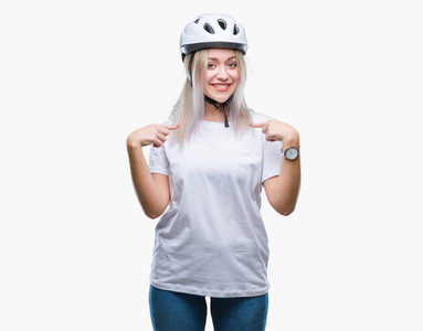 年轻的金发女子穿着自行车安全头盔在孤立的背景下, 脸上露出自信的笑容, 用手指自豪和快乐地指着自己。