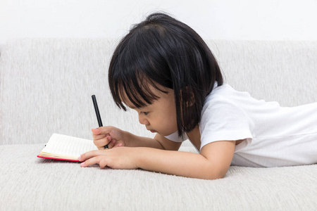 亚洲中国的小女孩躺在沙发上写作本书