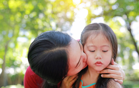 近距离的亚洲母亲亲吻她的女儿躺在夏天的花园