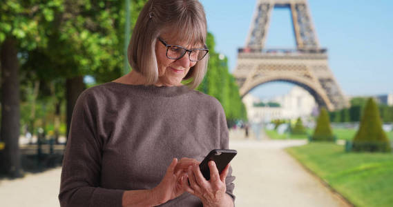 可爱的成熟的女人由埃菲尔铁塔使用智能手机设备发送短信