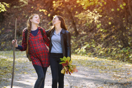 两个笑着的女人在公园里散步。秋天森林在距离
