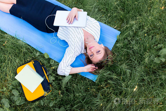 妇女休息在公园躺在草地上的笔记本电脑和听音乐