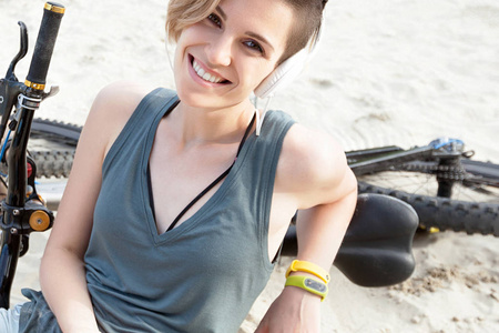 年轻的微笑的活跃的妇女坐在沙子与自行车。生活方式, 积极和积极