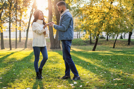 在秋天的公园里, 年轻人把订婚戒指戴在未婚妻的手指上