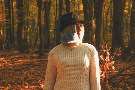 蓝色末端的金发女孩针织毛衣和帽子。秋天是温暖和阳光的气氛。金毛在森林里。自然背景