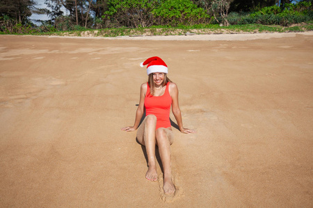 美丽的年轻女子与长头发在红色泳衣和圣诞老人帽子看着相机躺在普吉岛上的热带海滩上, 泰国