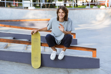 英俊的年轻滑板手坐在公园里的滑板的图像